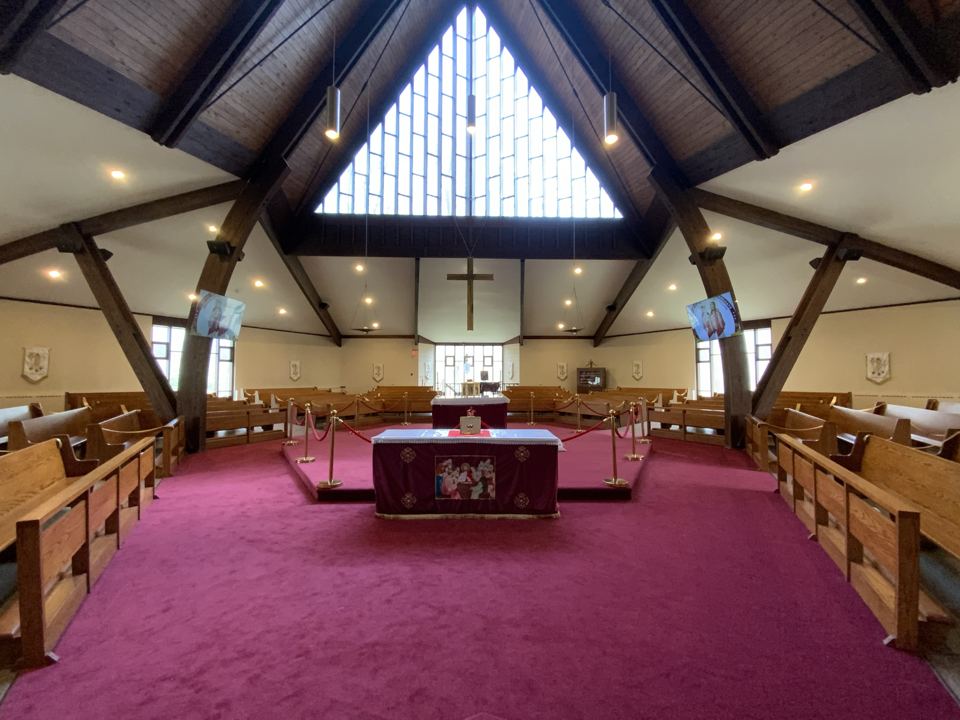 Inside the church: the altar at the center of the sanctuary, with seating around it and the tall triangular window above.