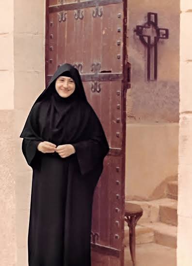 Tamav Irene in her black habit, smiling beside a wooden convent door